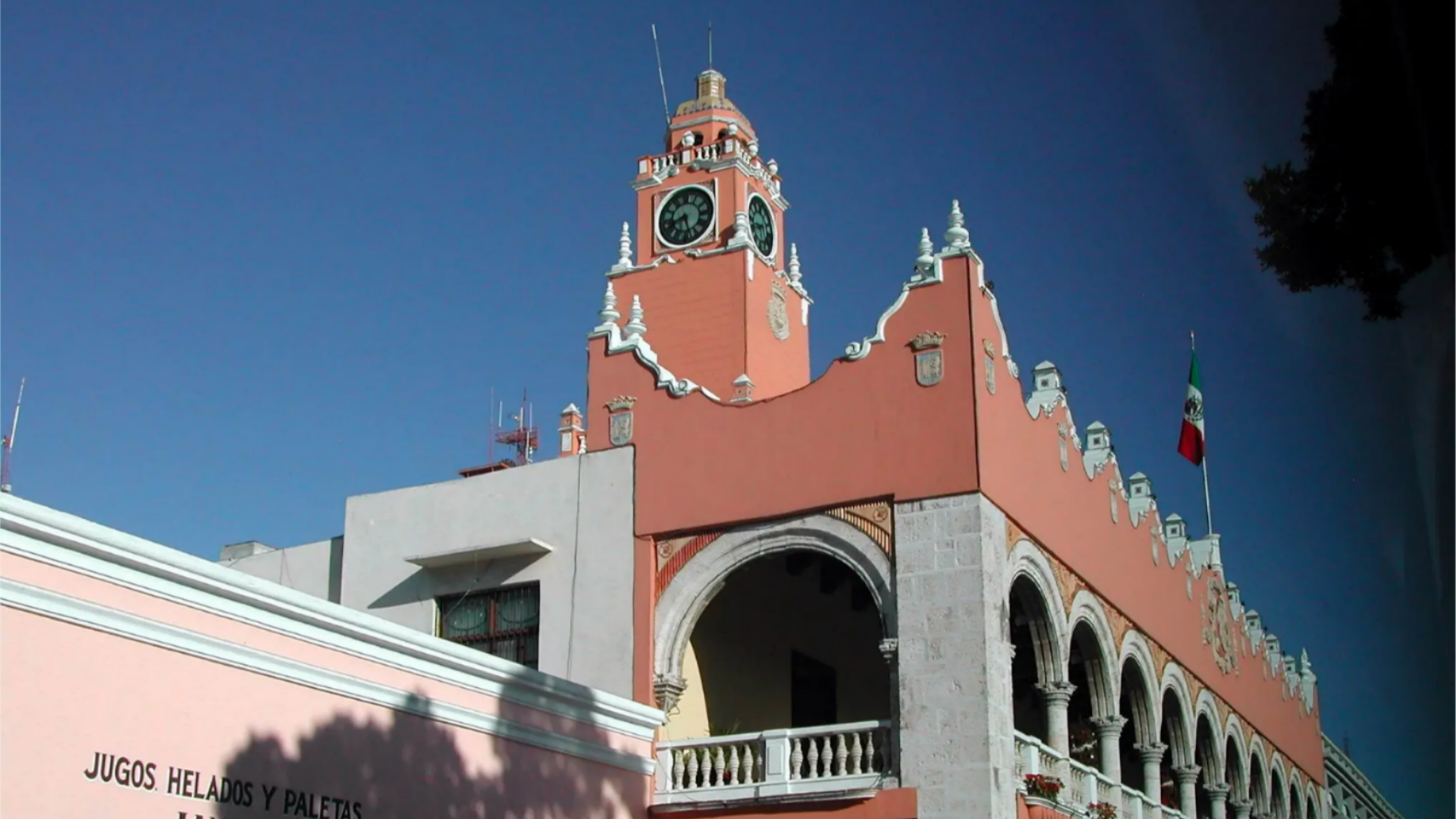 Coral building with Mexican flag before a blue sky